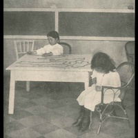 Una bambina conta la catena del <i>mille</i> ammassata sulla tavola; e l'altra, seduta in poltrona, conta la catena del <i>cento</i> [primi anni Dieci] - M. Montessori, <i>L'autoeducazione nelle scuole elementari</i>, Roma, E. Loescher &amp; C. - P. Maglione e Strini, 1916.$$$154
